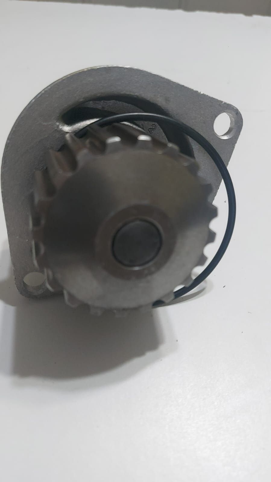 Primer plano de un engranaje o polea de metal gris con un soporte de montaje sobre una superficie blanca.