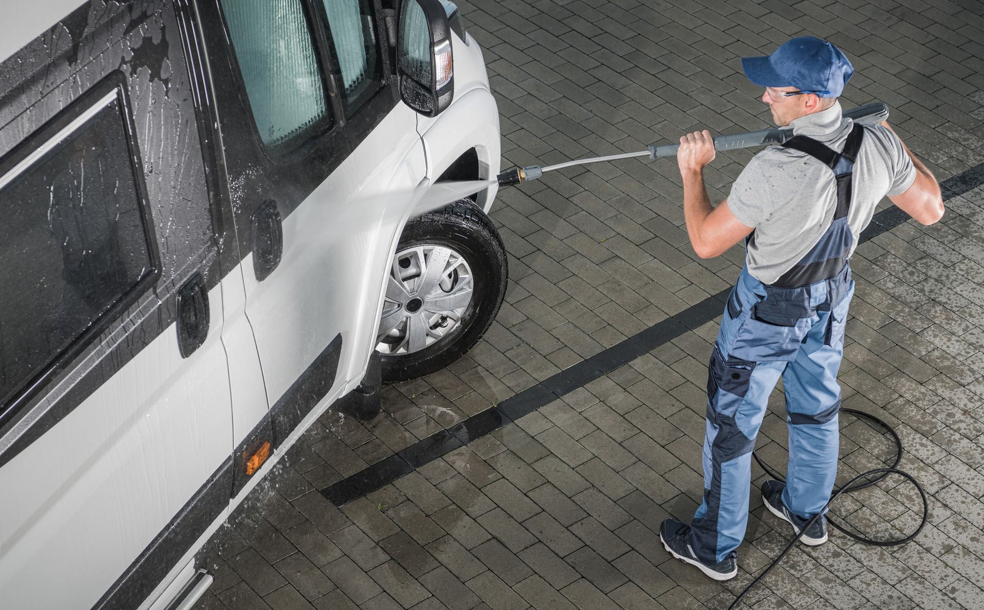 A man is washing a camper van with a high pressure washer.