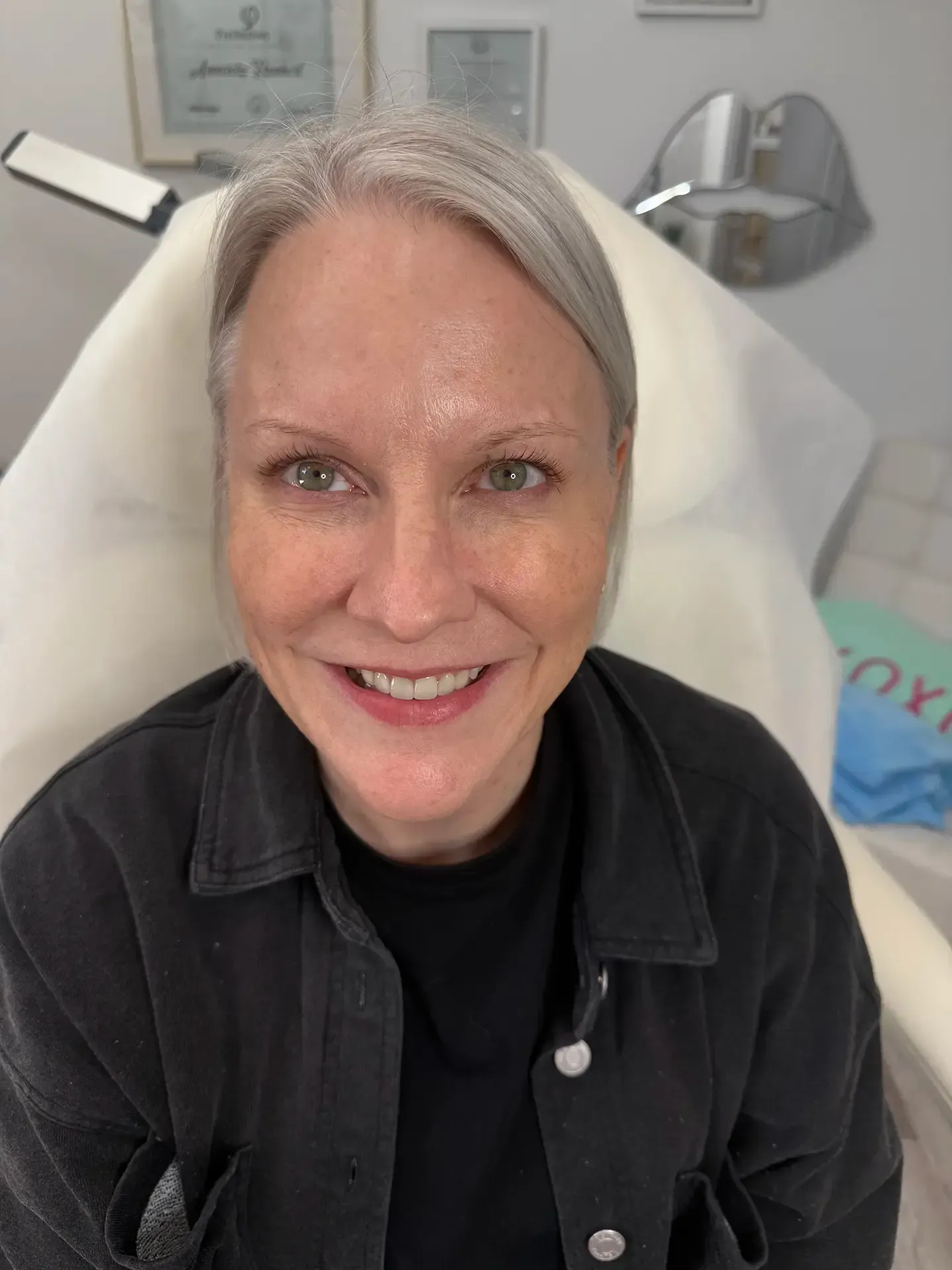 Woman with short gray hair smiles at the camera, sitting in a medical chair. 