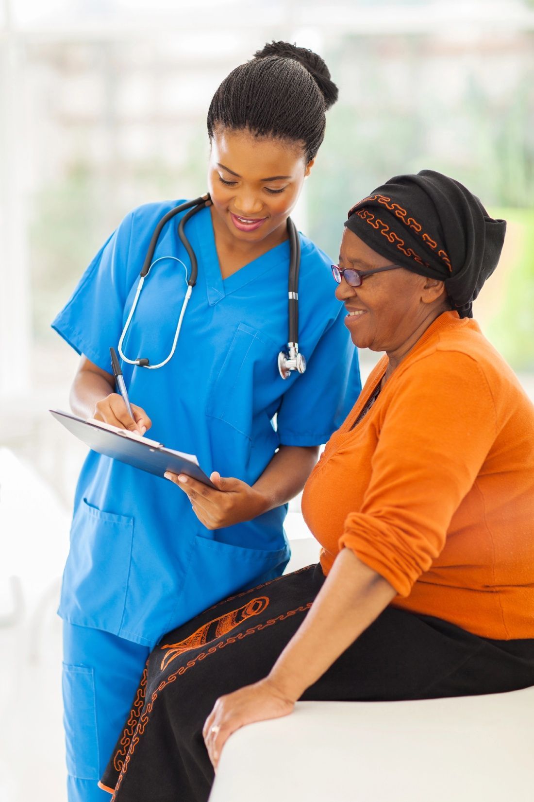 Nurse in blue scrubs with stethoscope reviews a clipboard with a patient in an orange shirt.