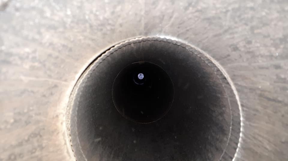 Vue de l'intérieur d'un tuyau ou d'un pot d'échappement en métal sombre, montrant une petite lumière vive et lointaine au centre.