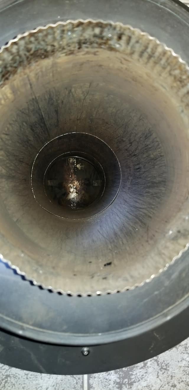 Vue en plongée de l'intérieur d'un tuyau d'échappement métallique circulaire et poussiéreux, montrant l'accumulation de suie et une ouverture sombre à sa base.