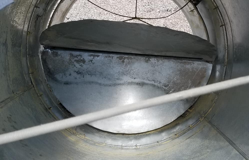 Intérieur d'un conduit d'air métallique avec un clapet ou un volet semi-circulaire obstruant partiellement l'ouverture de ventilation.
