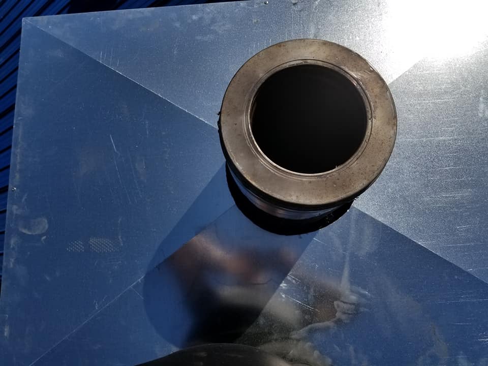Vue de dessus d'un raccord de tuyauterie cylindrique et sombre, centré sur une surface métallique plane et réfléchissante.