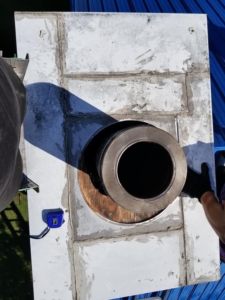 Vue de dessus d'un chapeau de cheminée sur un toit blanc, montrant un conduit de cheminée en acier inoxydable et un ruban à mesurer bleu.