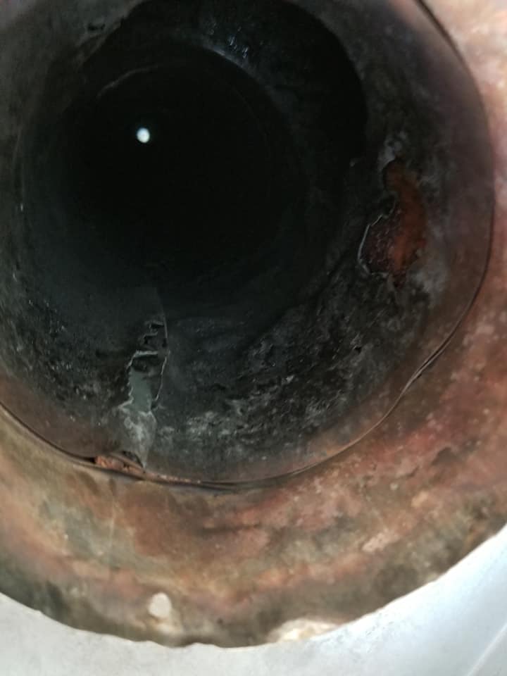 En regardant à l'intérieur d'un tuyau cylindrique sombre, on constate une importante corrosion interne, de la rouille et des dépôts noirs.