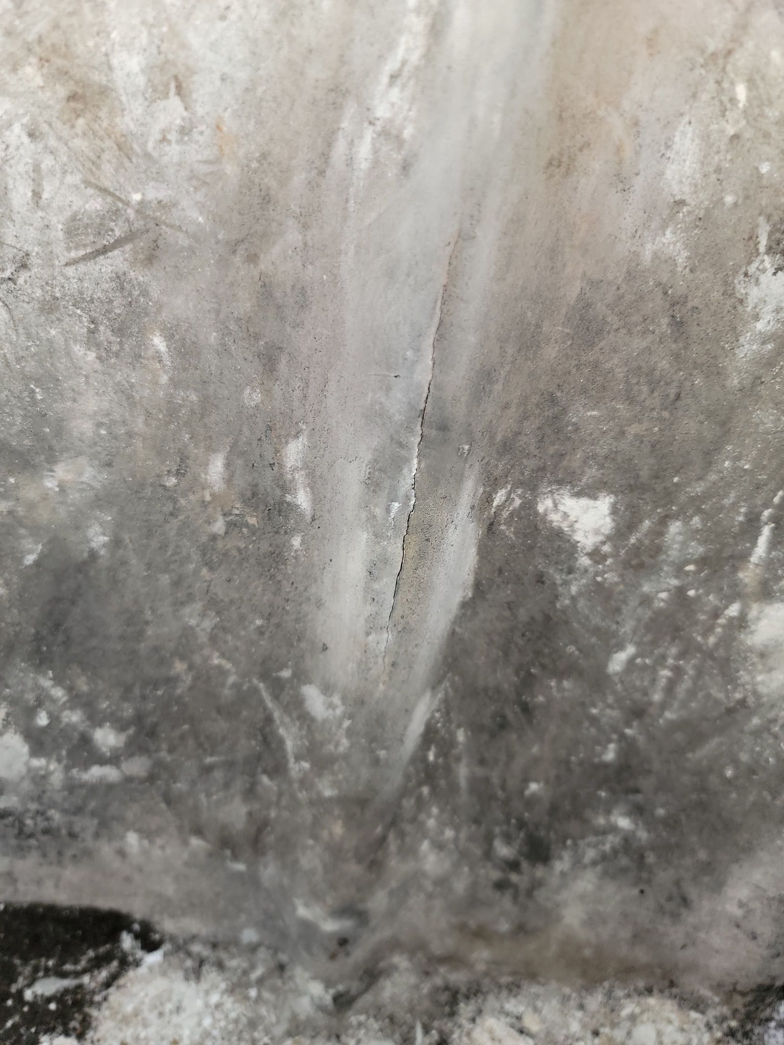 Une fissure verticale dans un mur en béton gris, marquée par des dépôts minéraux blancs et une décoloration due à des infiltrations d'eau.