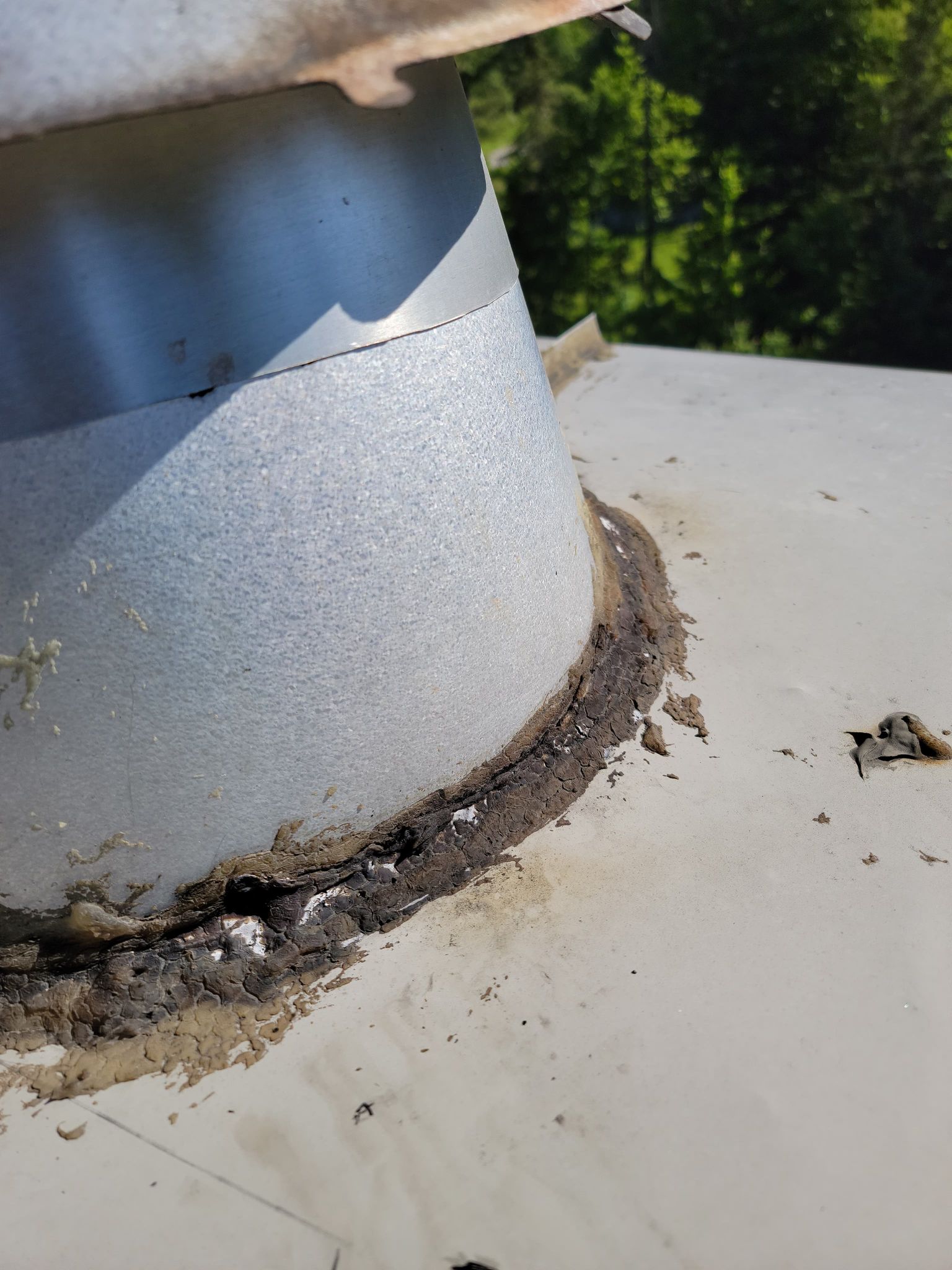 Gros plan sur un tuyau de ventilation de toit montrant des espaces importants et un mastic détérioré à la base, là où il rejoint la toiture.