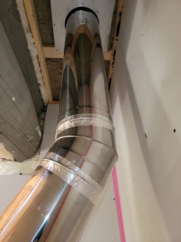 Un tuyau de ventilation métallique vertical à deux joints angulaires, remontant à travers une ouverture de plafond encadrée et non finie.