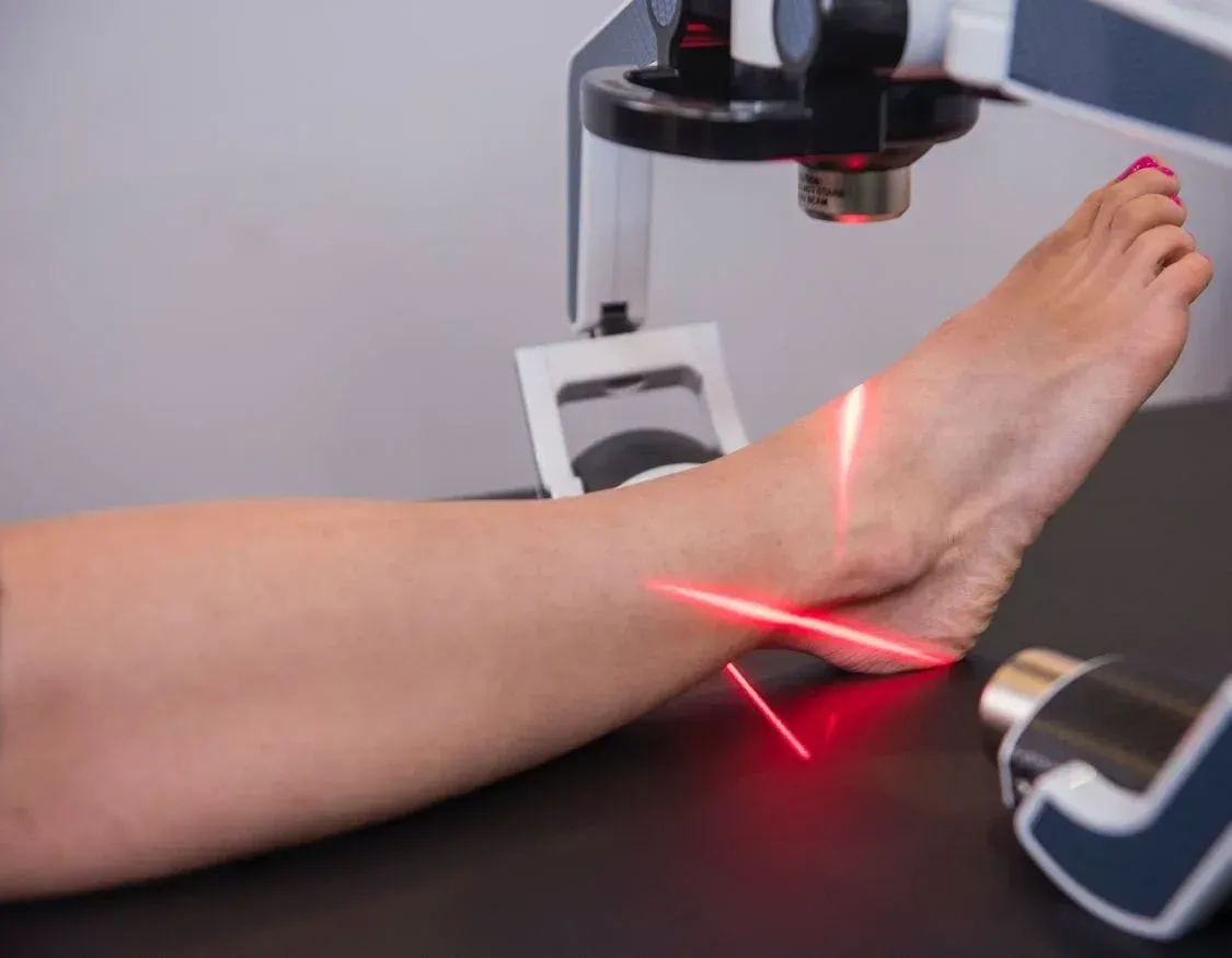 Laser therapy on a person's ankle; red laser beams target the area.