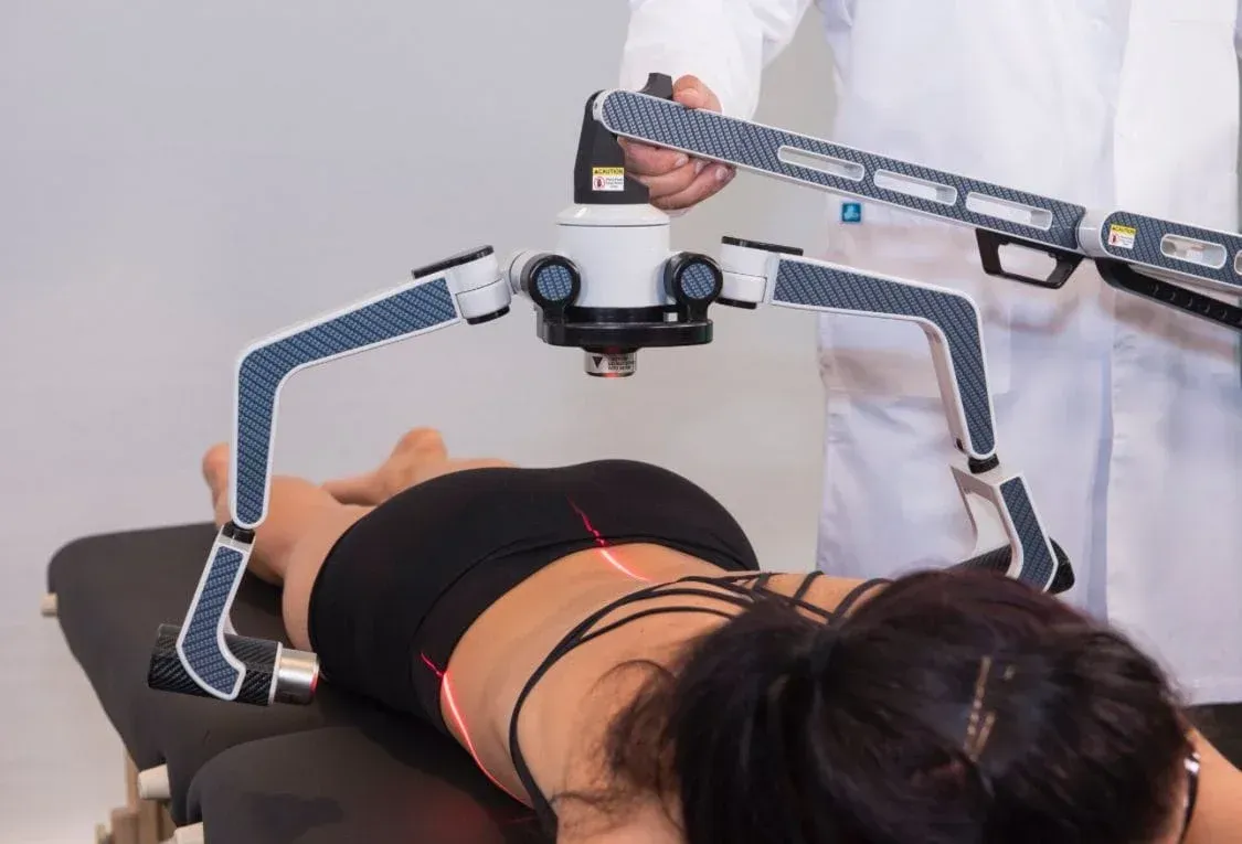 Woman undergoing spine scan using a medical device in a doctor's office. Red lasers indicate the scanning area.