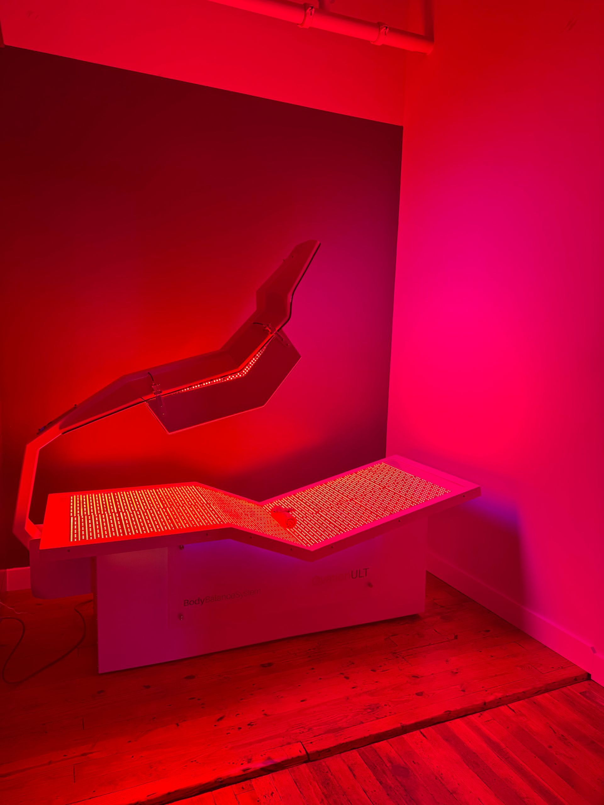 Red light therapy device in a pink-lit room, used for health and wellness treatments.
