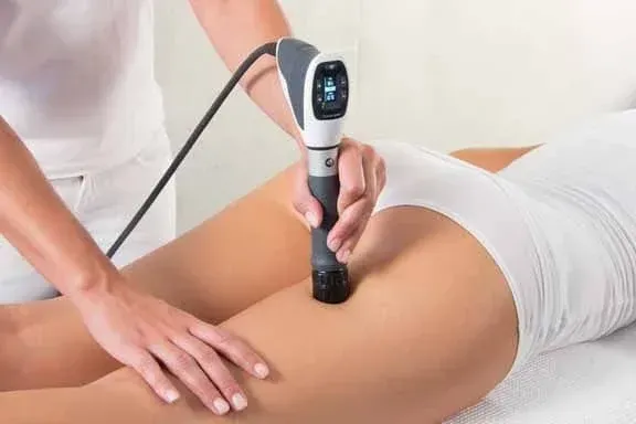 Woman receiving a treatment to her thigh with a handheld medical device.