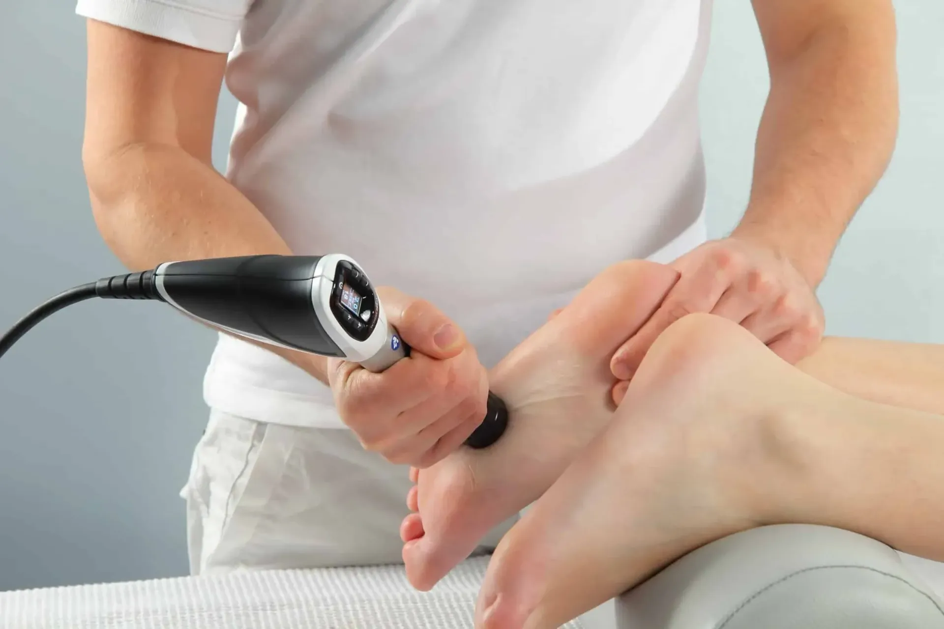 A person receives foot therapy; device held on the foot. Practitioner is in white.