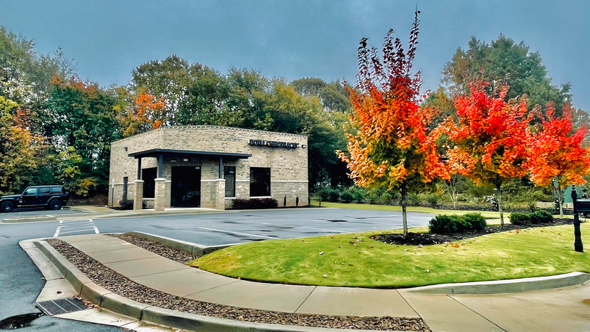 Building with stone facade and trees with fall foliage. Driveway and landscaping in front.