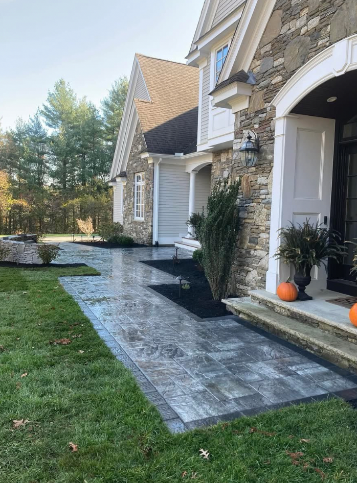 Stone walkway leading to a house with stone and gray siding. Green grass and fall pumpkins.