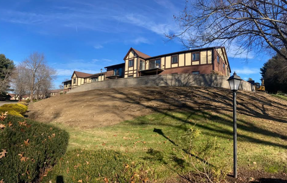 A Tudor-style building on a hillside under a bright blue sky. Brown and tan exterior with a grassy foreground.