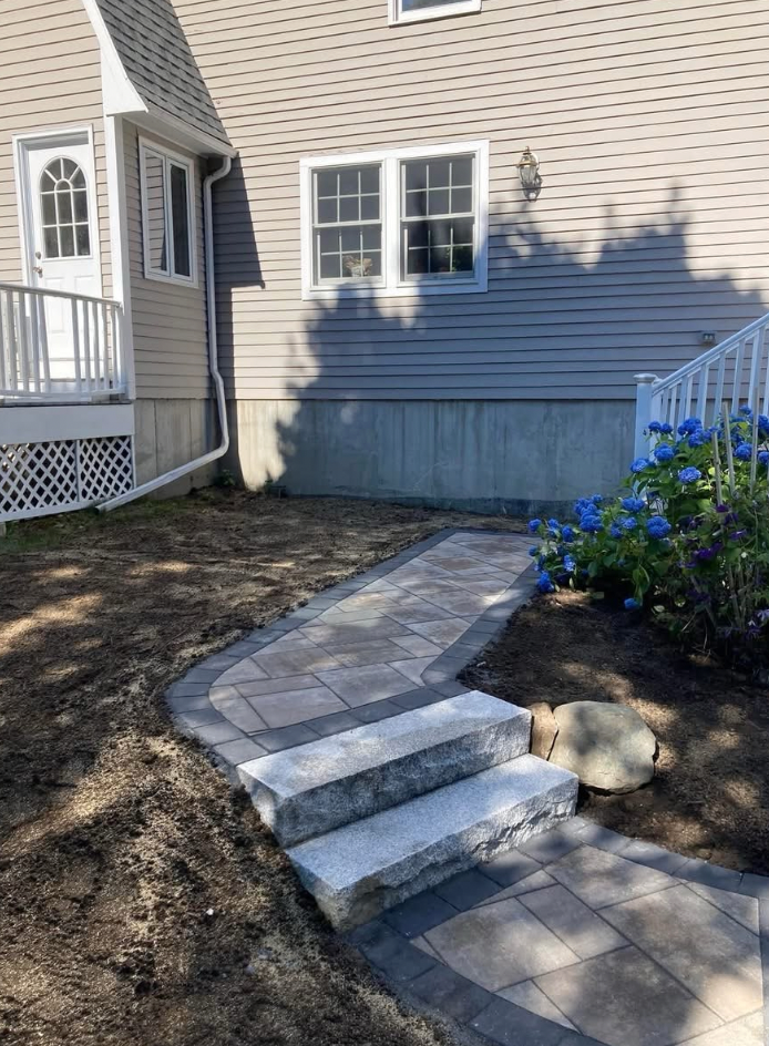 Stone pathway with steps leading to a house with blue siding, a door, and windows.