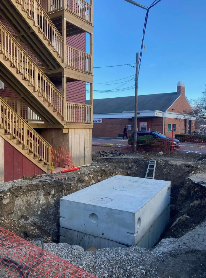 Concrete septic tank in a construction site near an apartment building and a commercial building.