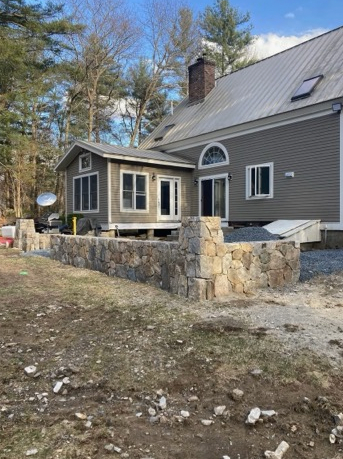 Stone wall and extension added to a house. Gray siding, arched window.