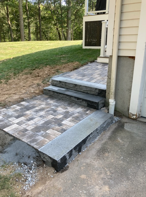 Brick patio with steps leading up to a deck; gray and brown bricks, gray steps.