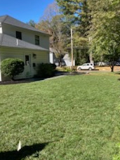 A well-manicured green lawn next to a two-story white house with a car parked on the street.