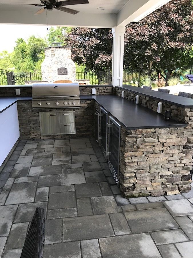 Outdoor kitchen with stone facade, grill, refrigerator, and a countertop under a covered patio.