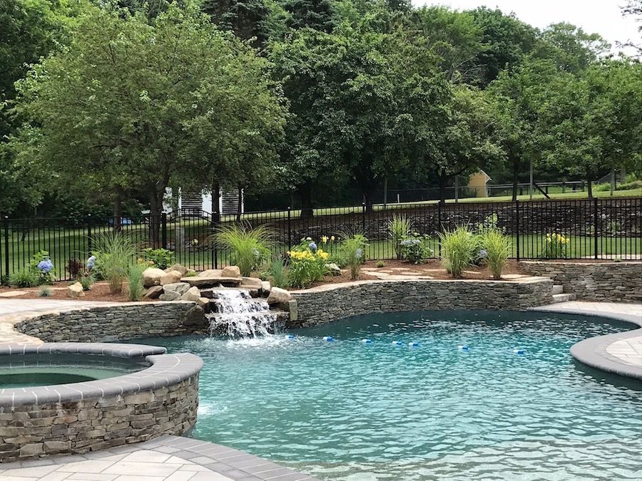 Swimming pool with waterfall, landscaping, and stone walls.