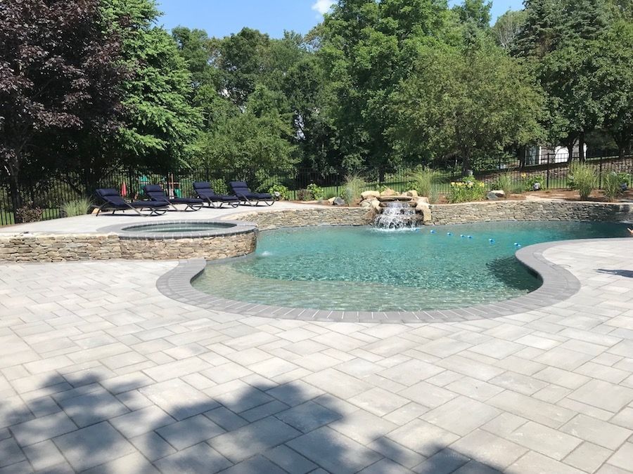 Backyard pool with waterfall and stone patio on a sunny day.
