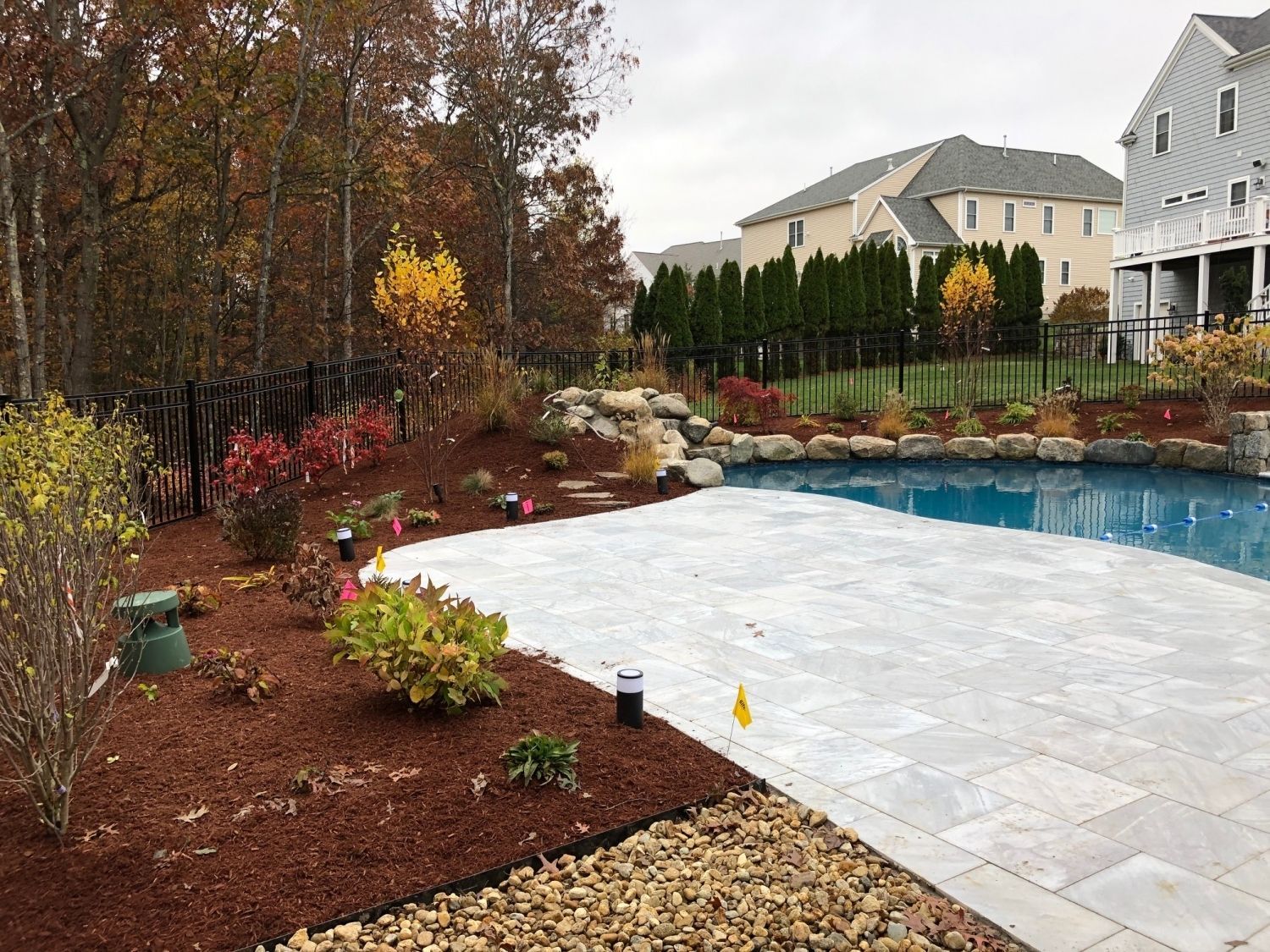 Backyard pool with patio, landscaping, and fall foliage; houses in the background.