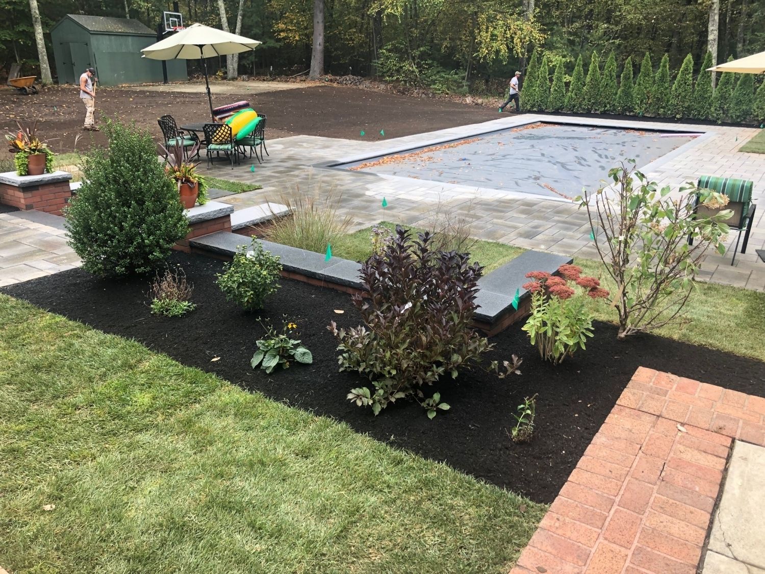 Backyard with pool, landscaped beds, and patio. People visible.