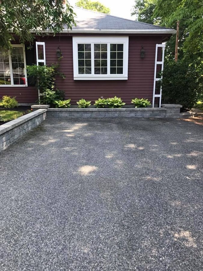 Red house with white trim, small retaining wall with shrubbery, paved driveway.
