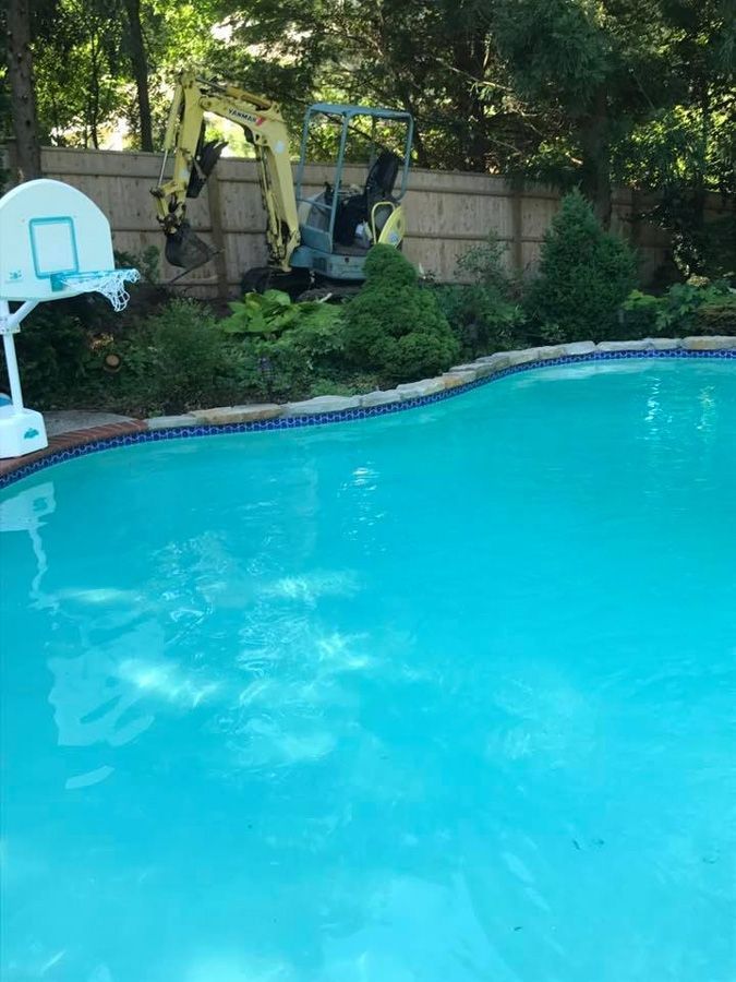 Pool with blue water and a small excavator by a fence.