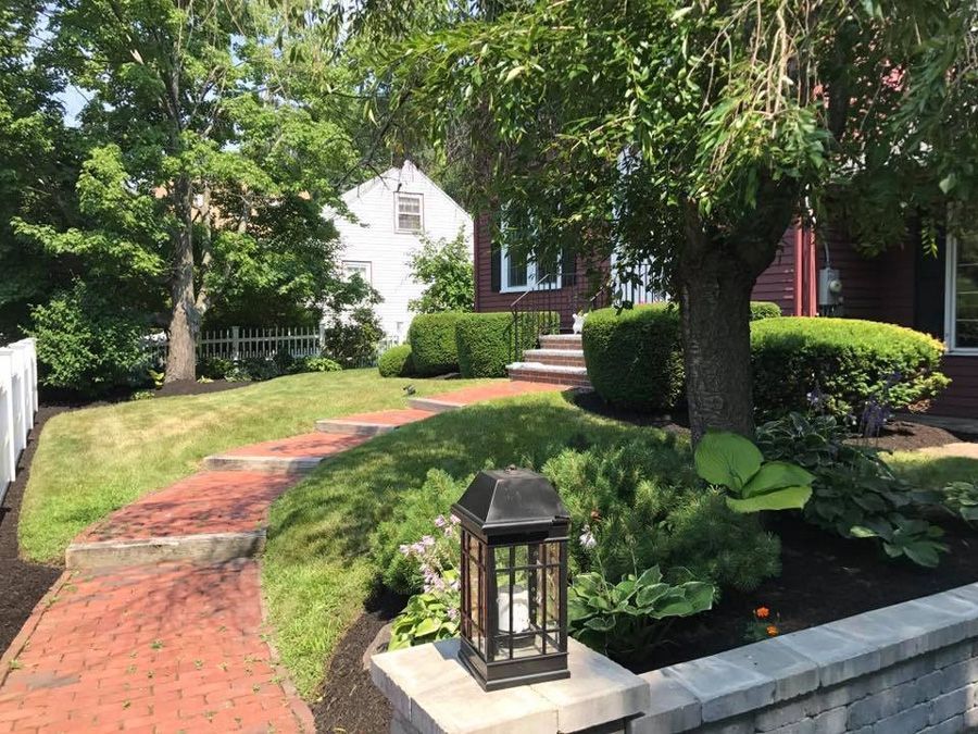 Brick path leading up to a red house with landscaping and a lantern.