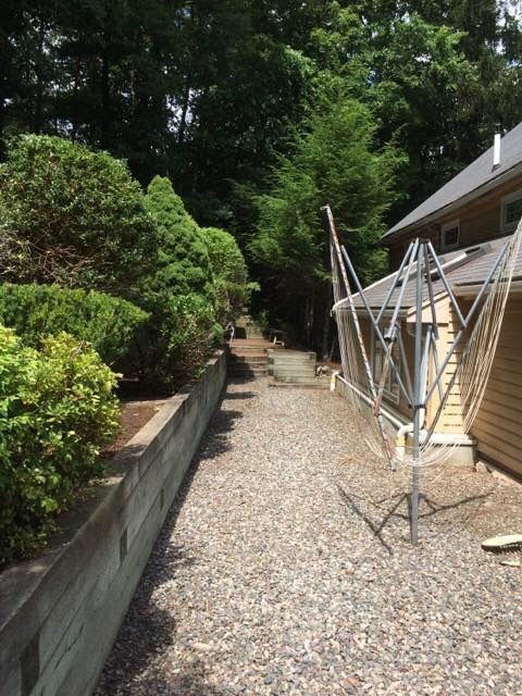 Gravel path next to house and raised garden bed. Trees border the path, with a clothesline on the right.