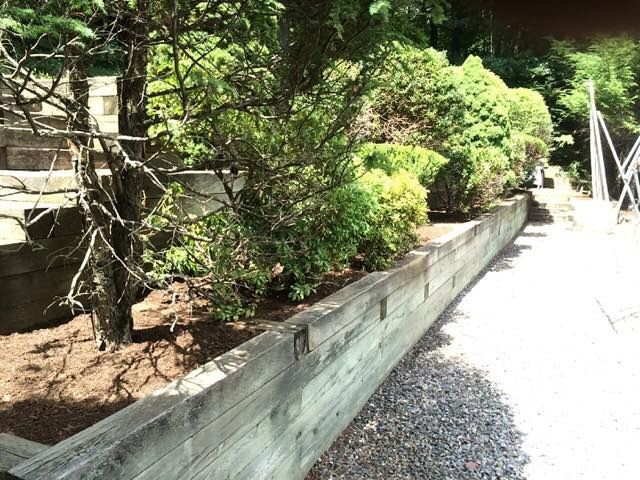Wooden retaining wall with shrubs, beside a gravel path.
