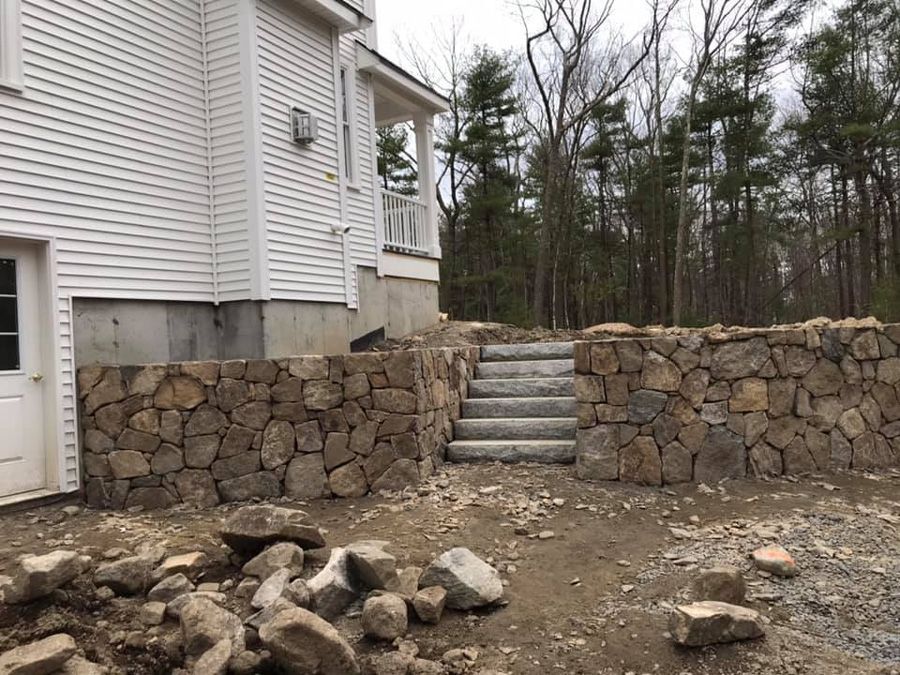 Stone retaining walls and steps leading up to a house with white siding and a small porch.