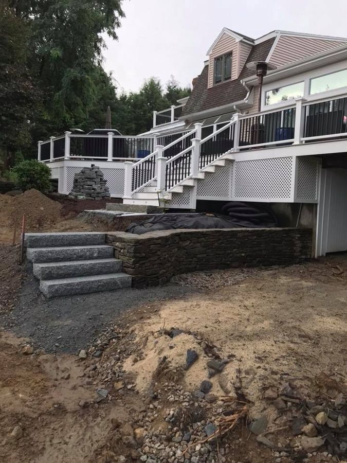 Stone steps leading up to a multi-level deck attached to a house with white trim and black railings.