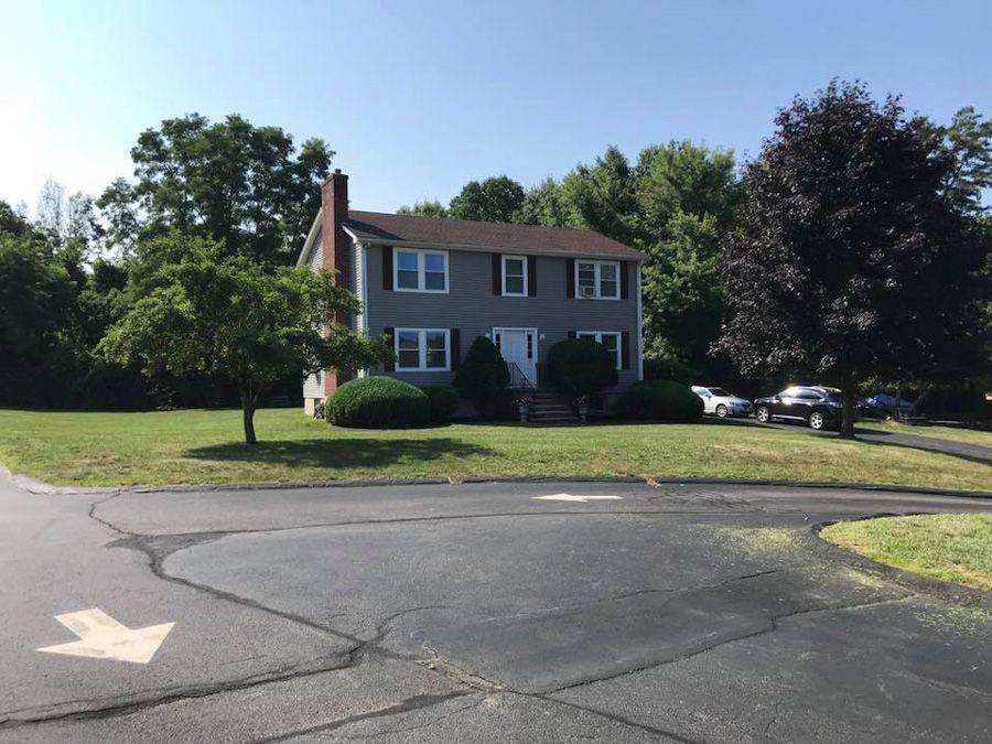 Two-story gray house with black roof, surrounded by trees, on a sunny day.
