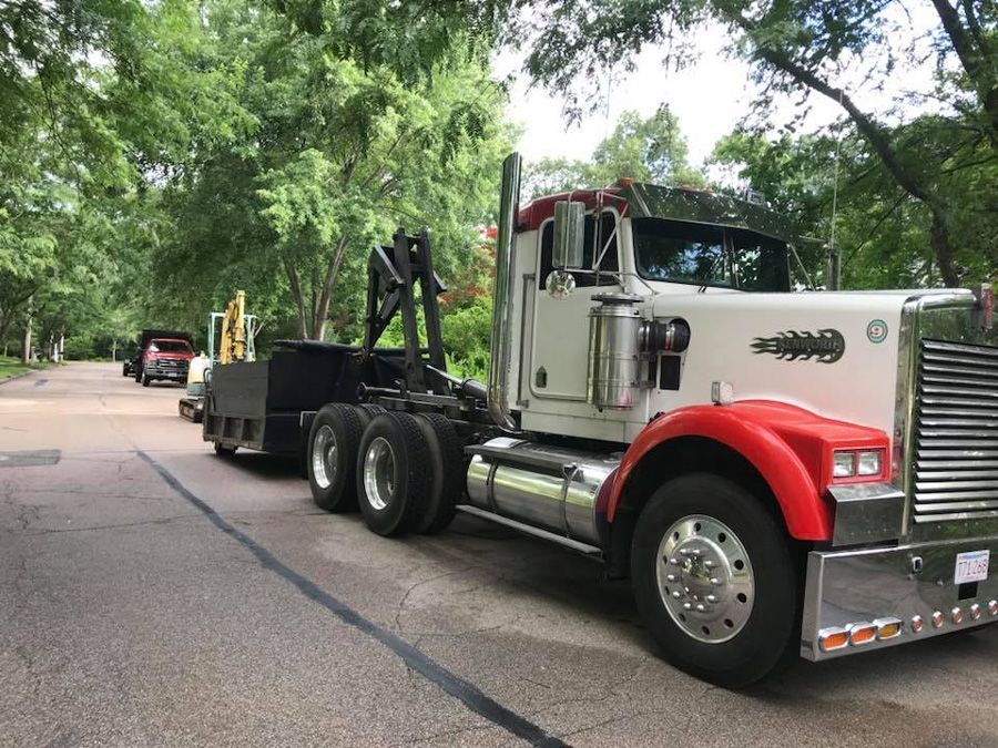 A large white and red semi-truck with a trailer on a tree-lined street.