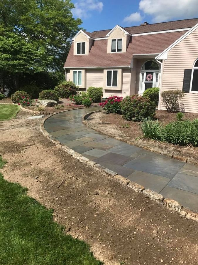 Stone walkway leading to a light pink house with a brown roof.