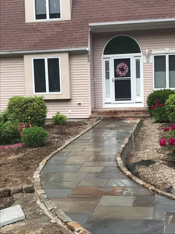 A stone pathway leads to a home's arched doorway, flanked by landscaping and flowers.