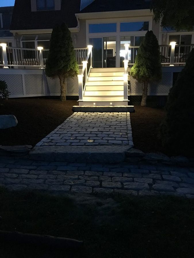 Stone pathway leads to lit stairs and house at night.