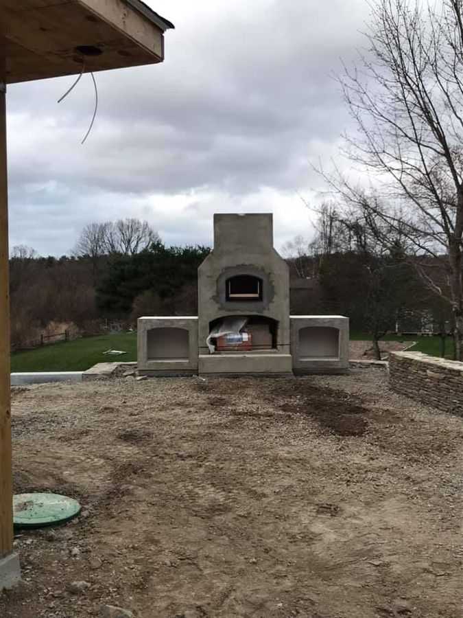 Outdoor pizza oven with concrete structure on a gravel patio, cloudy sky background.