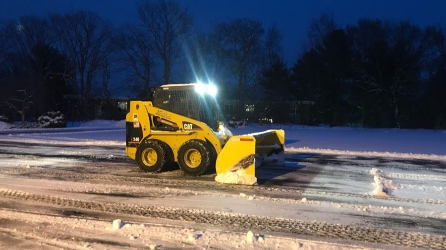 Yellow skid steer with snowblower clearing snow at night.
