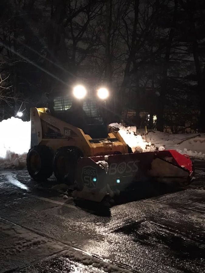 Yellow snowplow with BOSS blade clearing snow at night.