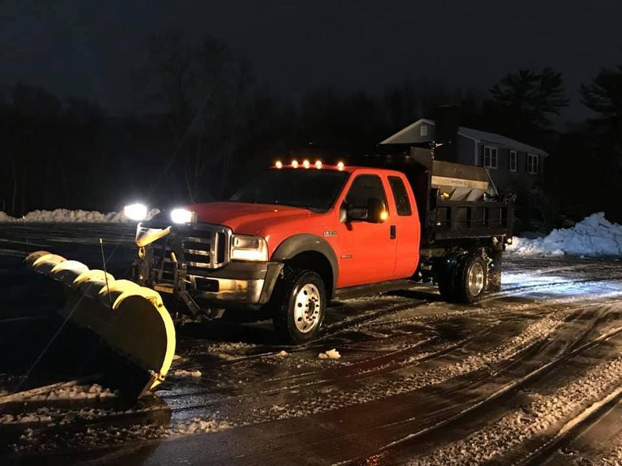 Red pickup truck with snowplow clearing a driveway at night.