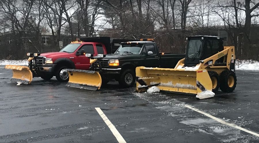 Three snowplows parked on a snowy parking lot, ready to clear snow.