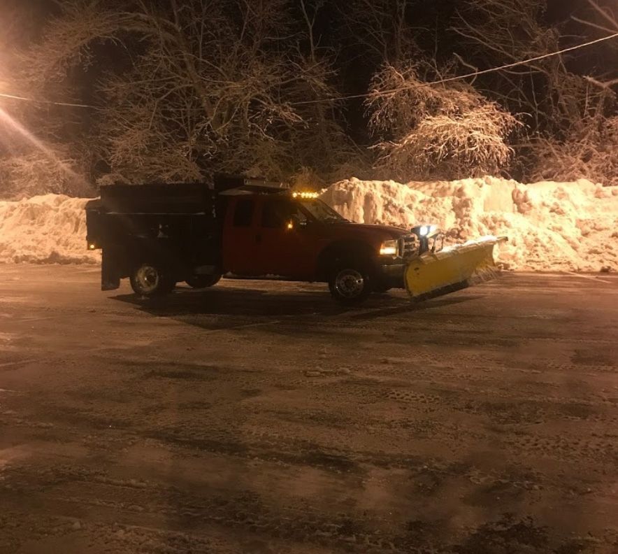 Red pickup truck plowing snow at night, with a pile of snow in the background.