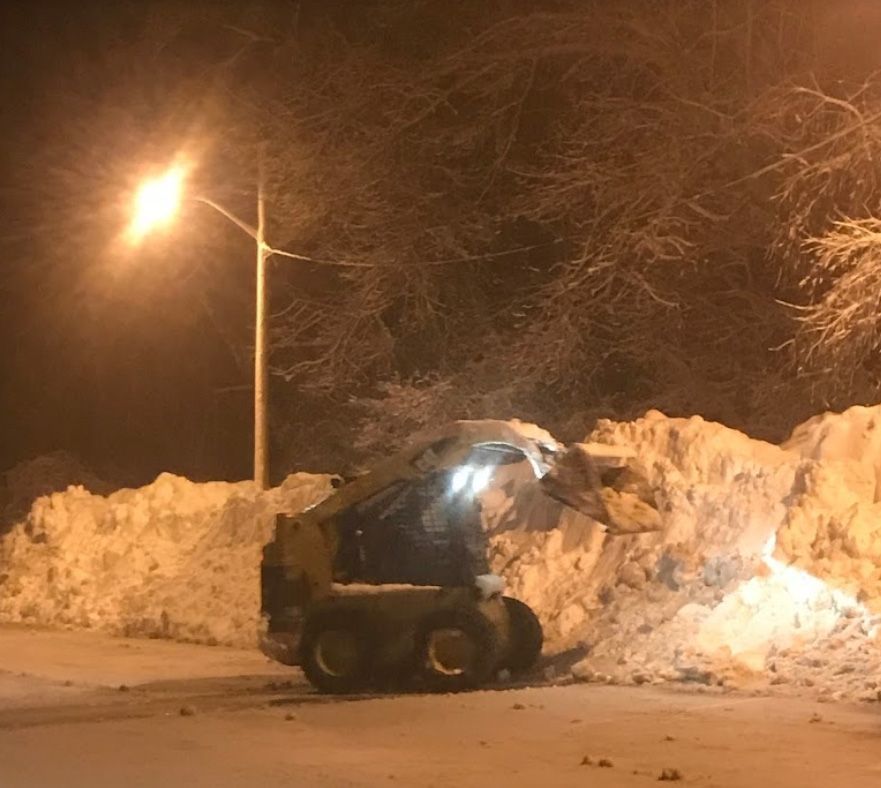 Snowplow pushing snow at night under a street light.